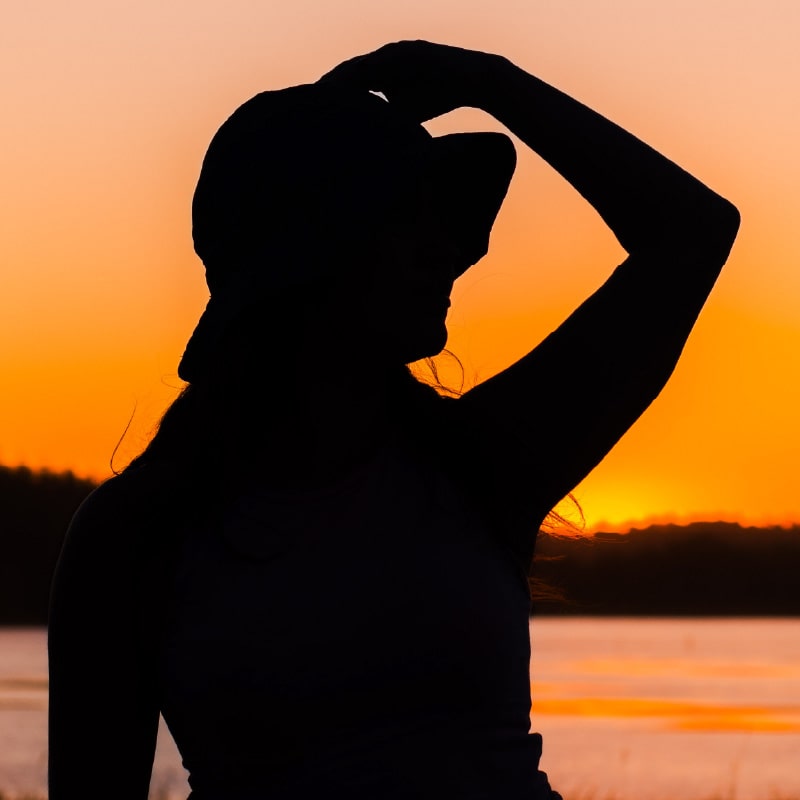 A silhouette of a woman wearing a hat as she looks out across the sea at sunset